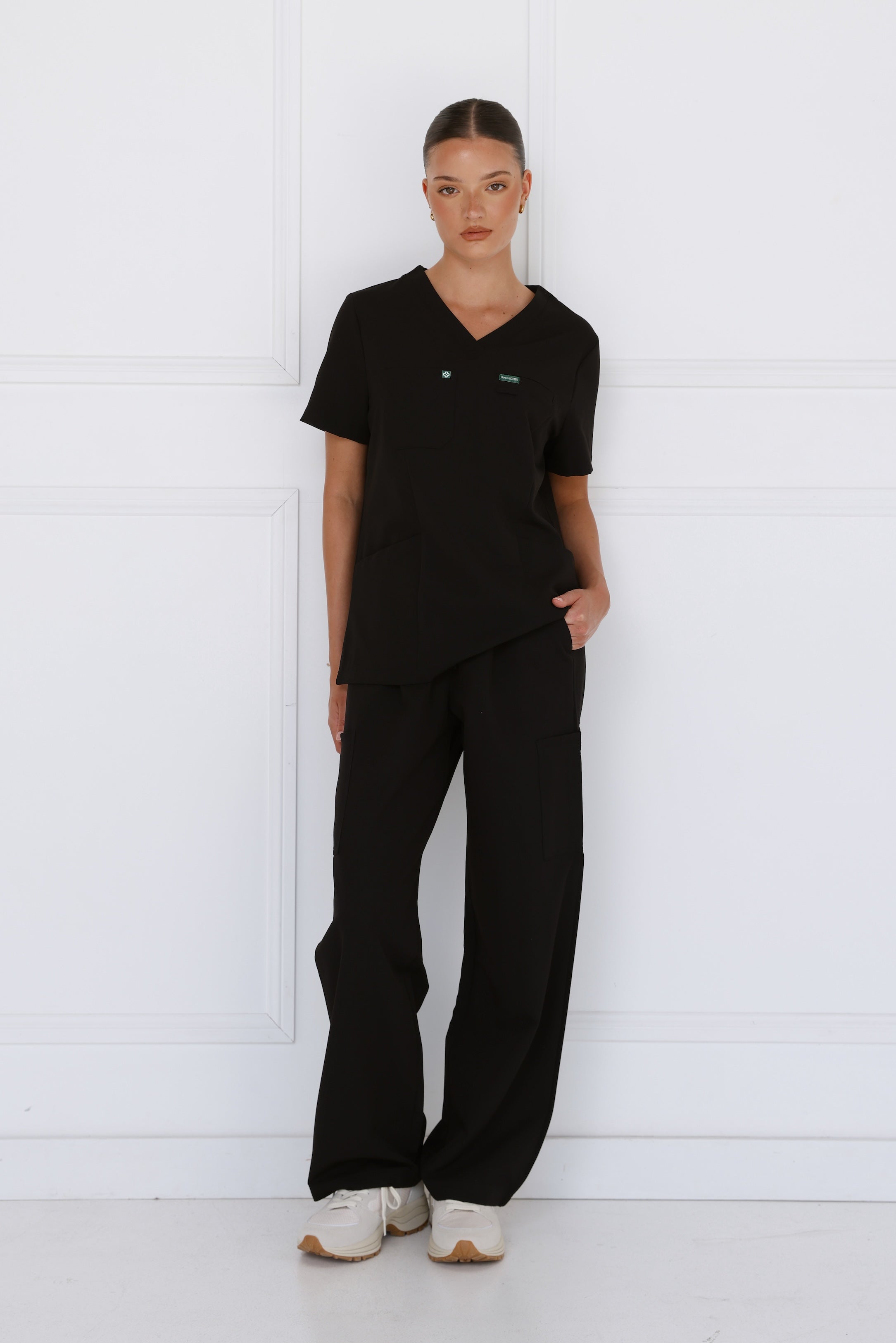Female model wearing the Hero Scrubs Black scrub set in solid black with a matching scrub top and scrub pants.