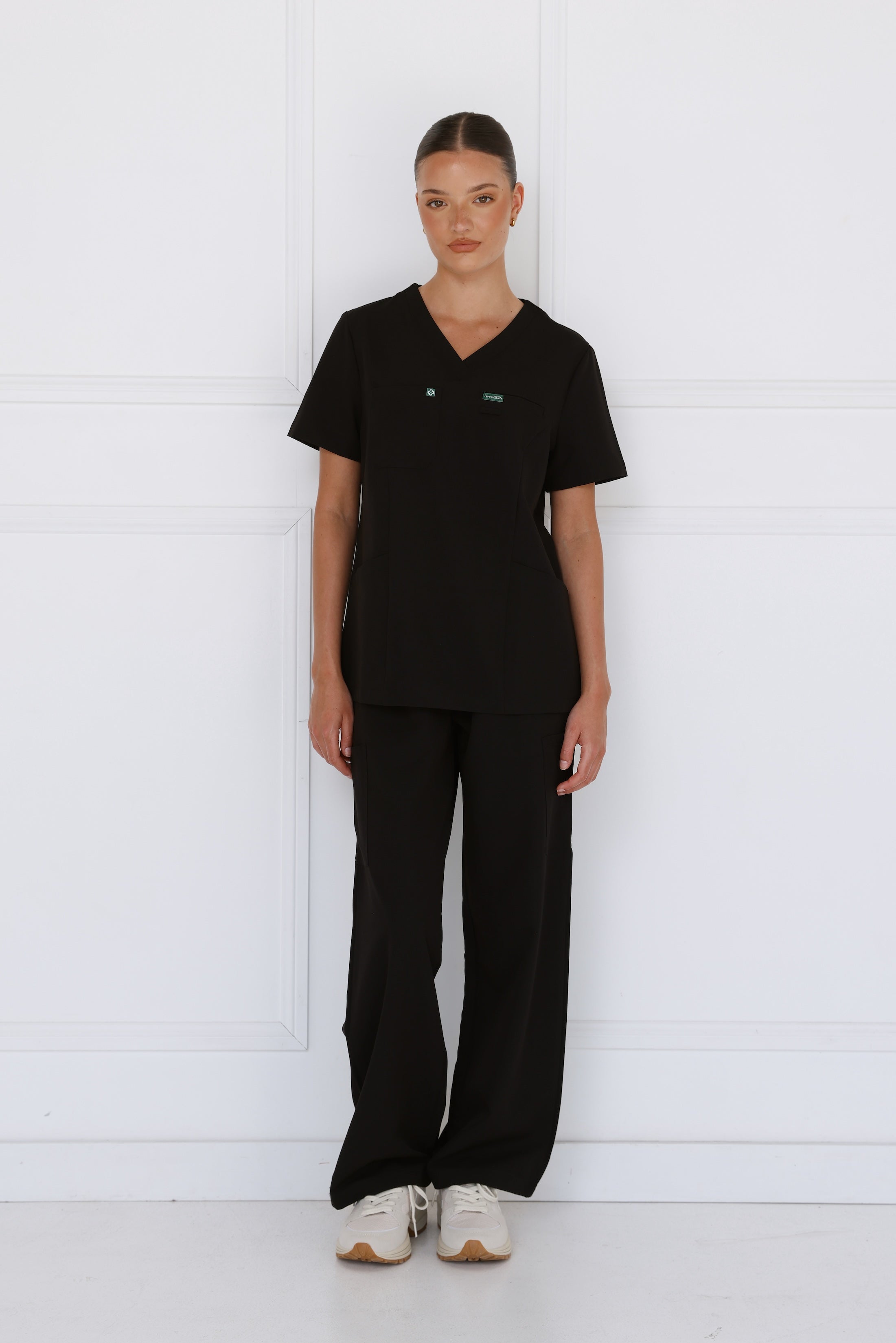 Front view of the Hero Scrubs Black scrub set on a female model showing the solid black colour, tailored fit and matching scrub pants.