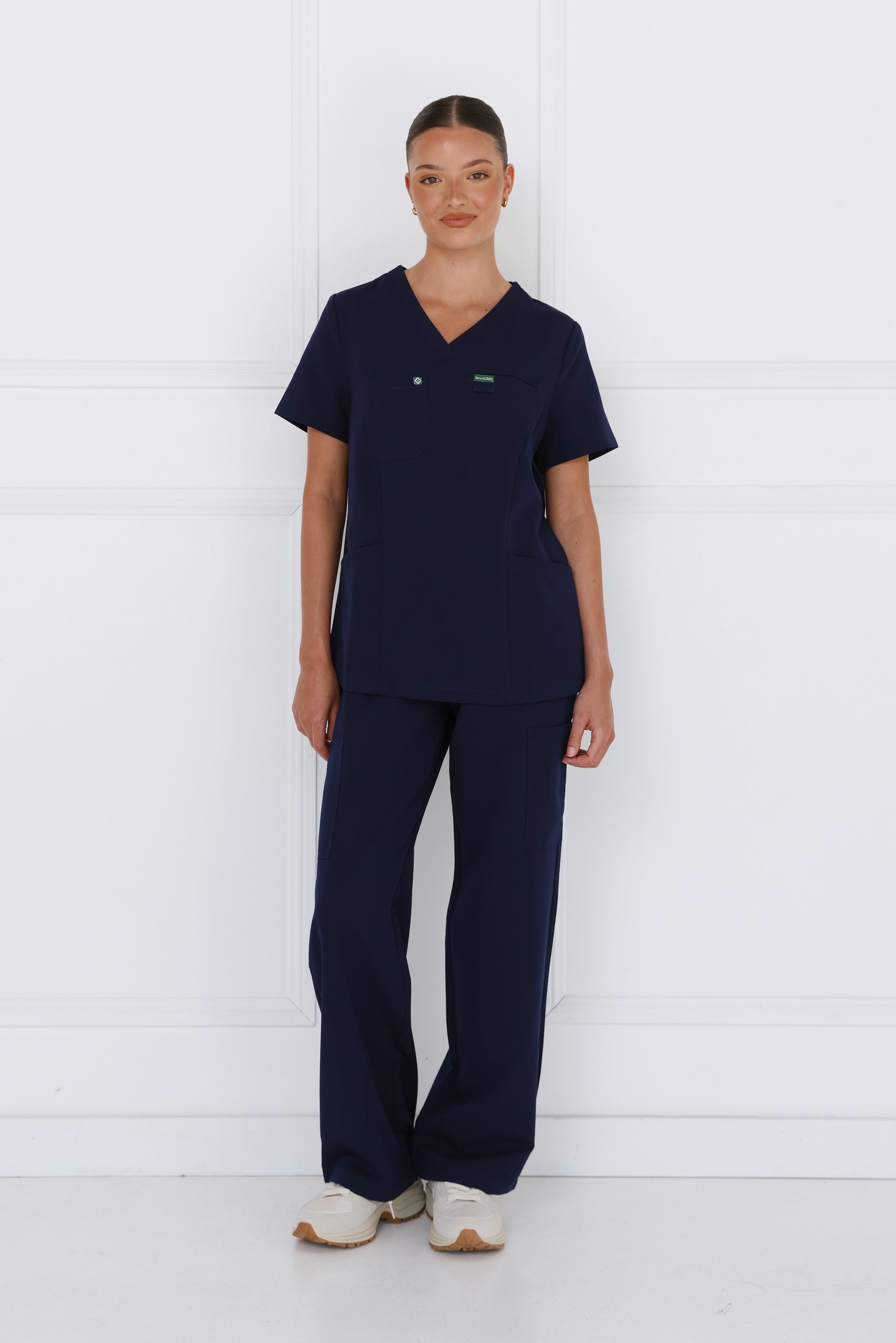 Female model wearing the Hero Scrubs Midnight Navy scrub set in a deep navy blue with a matching scrub top and scrub pants.