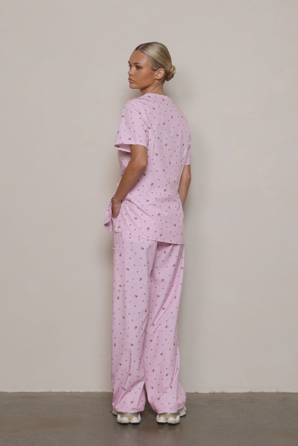 Model looking over her shoulder in a Hero Scrubs pastel pink floral scrub set, showing the side and back.