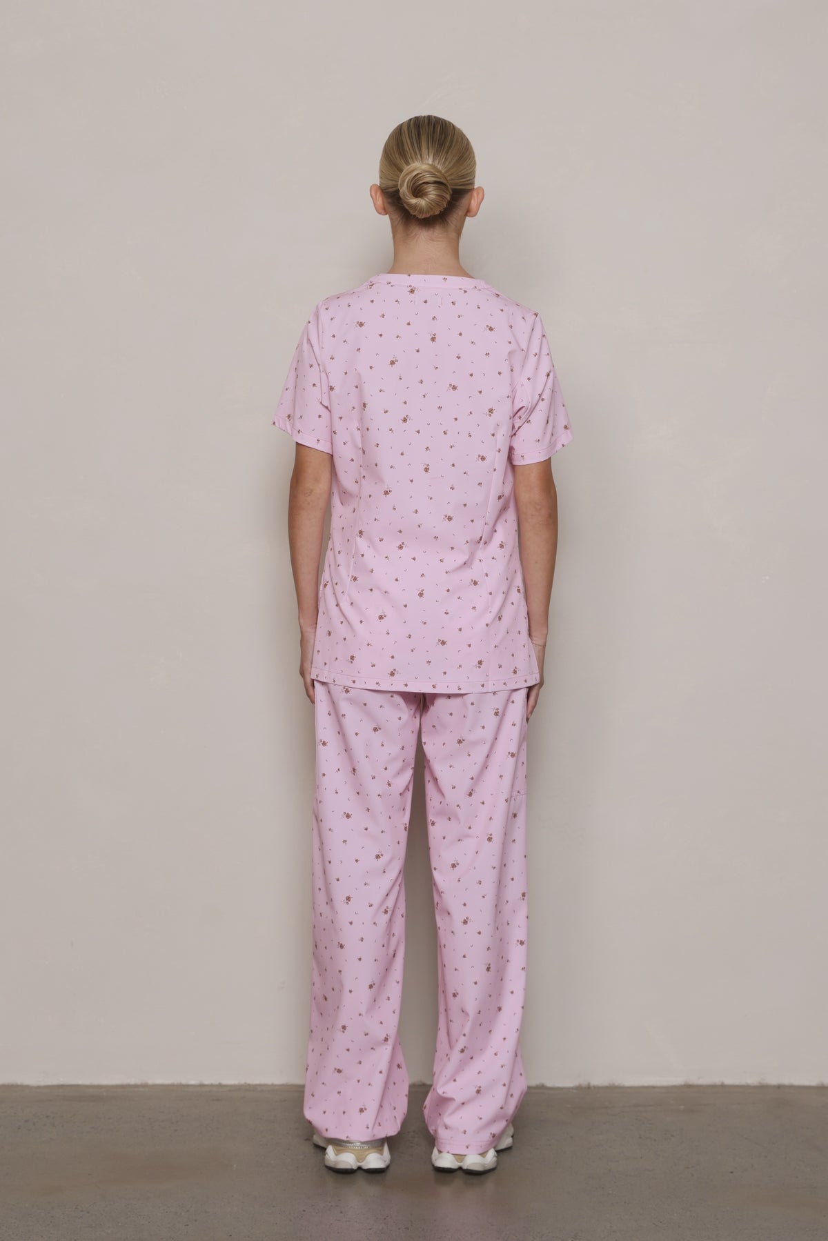 Back view of a model wearing a Hero Scrubs pastel pink floral top and matching pants.