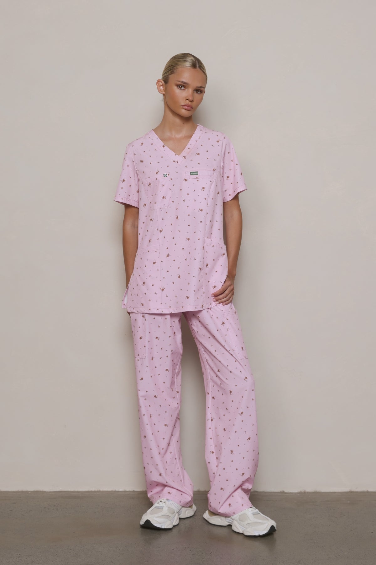 Model wearing a Hero Scrubs pastel pink scrub set with a small floral print, viewed from the front.