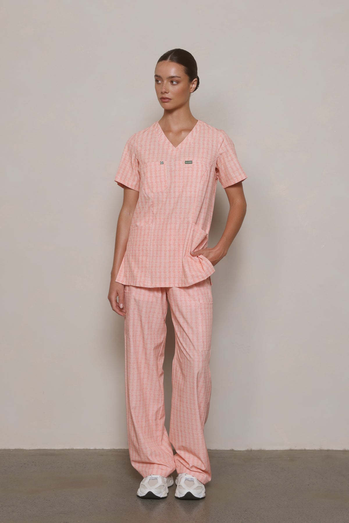 Model wearing a Hero Scrubs Peach Relaxed Back scrub set, standing at a slight angle with one hand in her pocket.