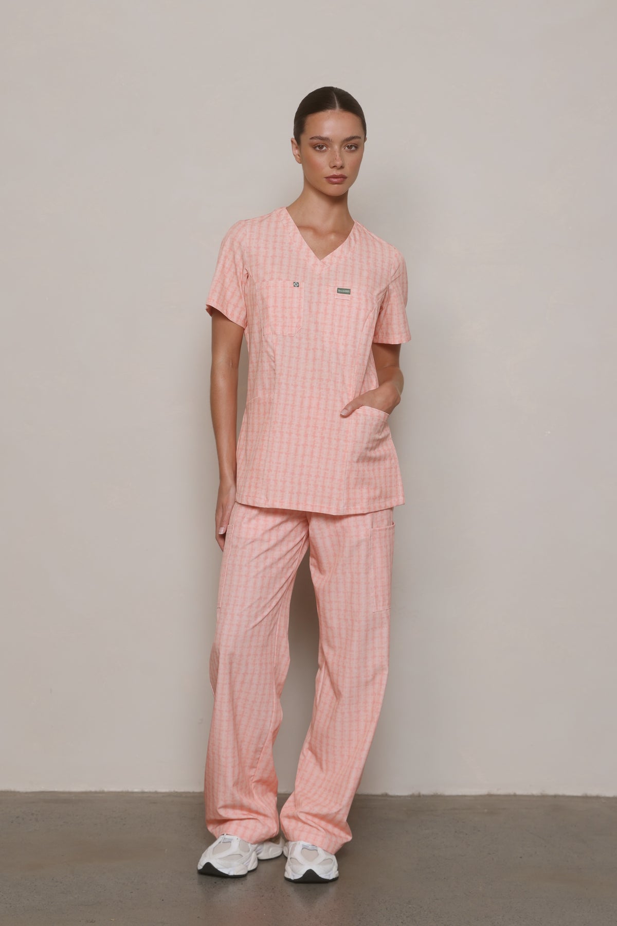 Model wearing a Hero Scrubs Peach Relaxed Back striped scrub set with one hand in her top pocket.