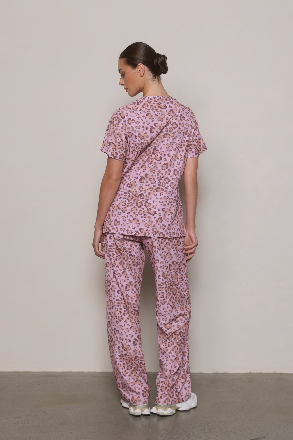 Model wearing a Hero Scrubs pink leopard-print scrub set, showing the back of the top and pants.