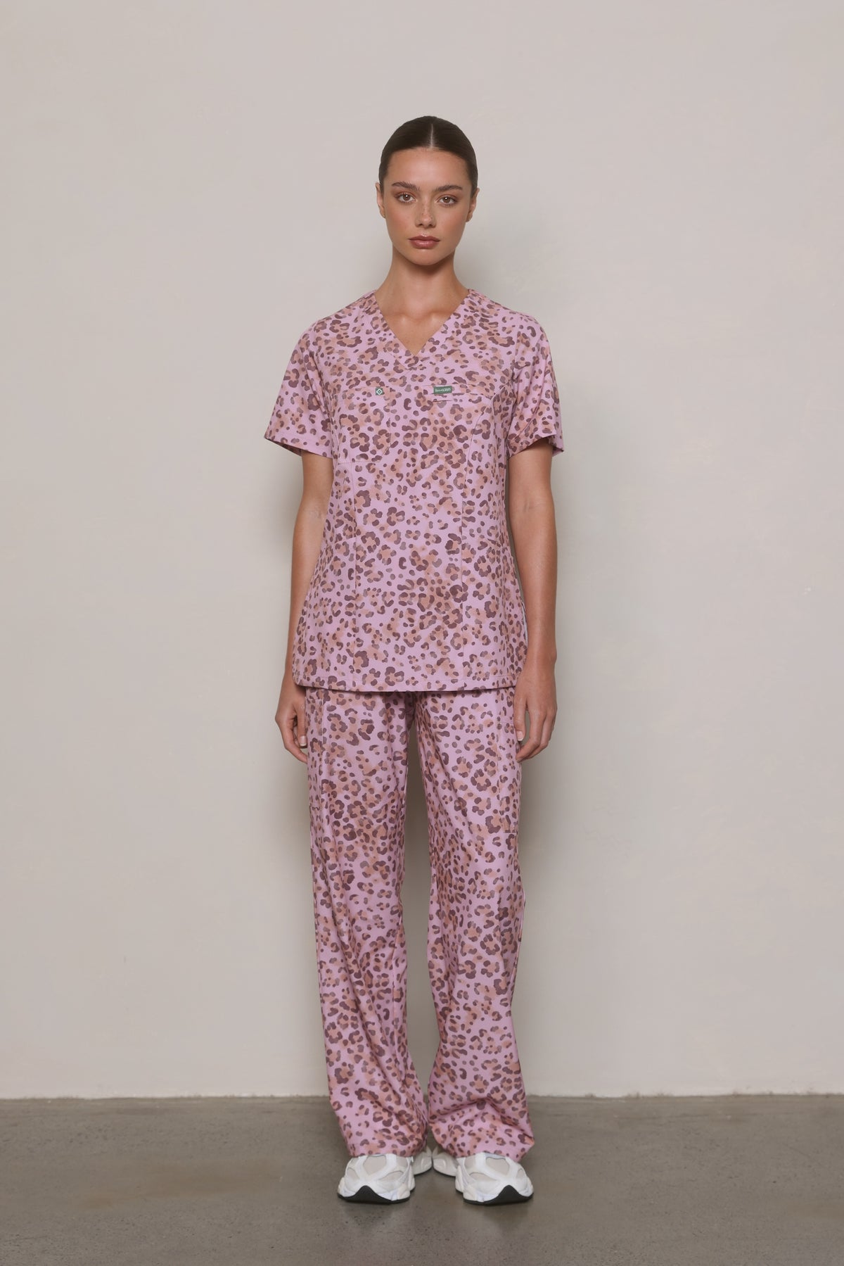 Model wearing a Hero Scrubs pink leopard-print V-neck top and matching pants, viewed from the front.
