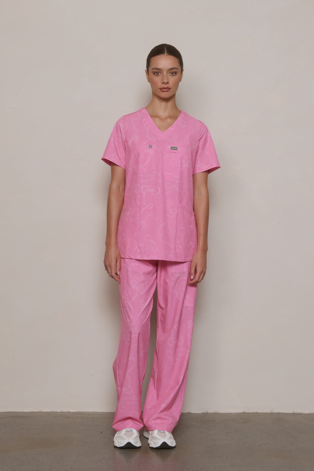 Model wearing a Hero Scrubs pink printed V-neck top and matching pants, viewed from the front.