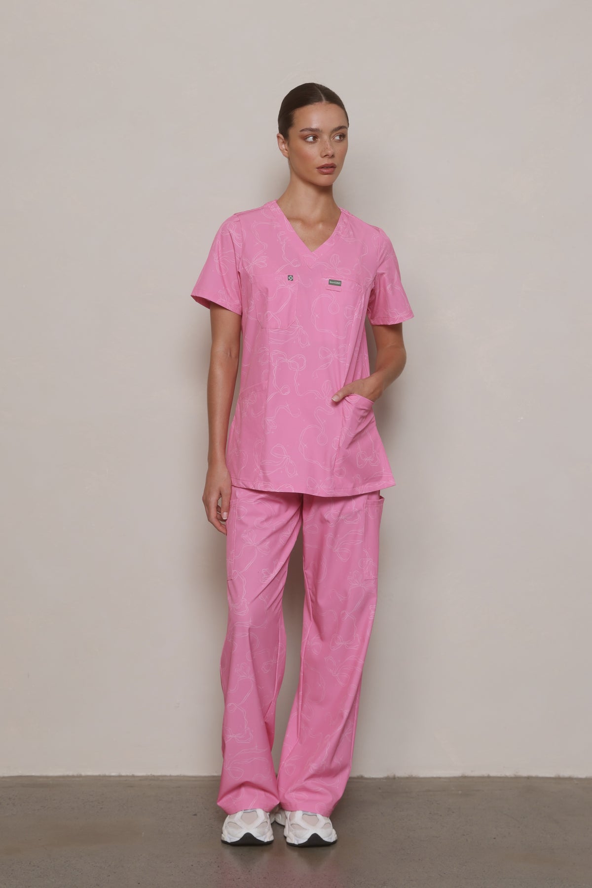 Model wearing a Hero Scrubs pink printed scrub set with one hand in her top pocket.