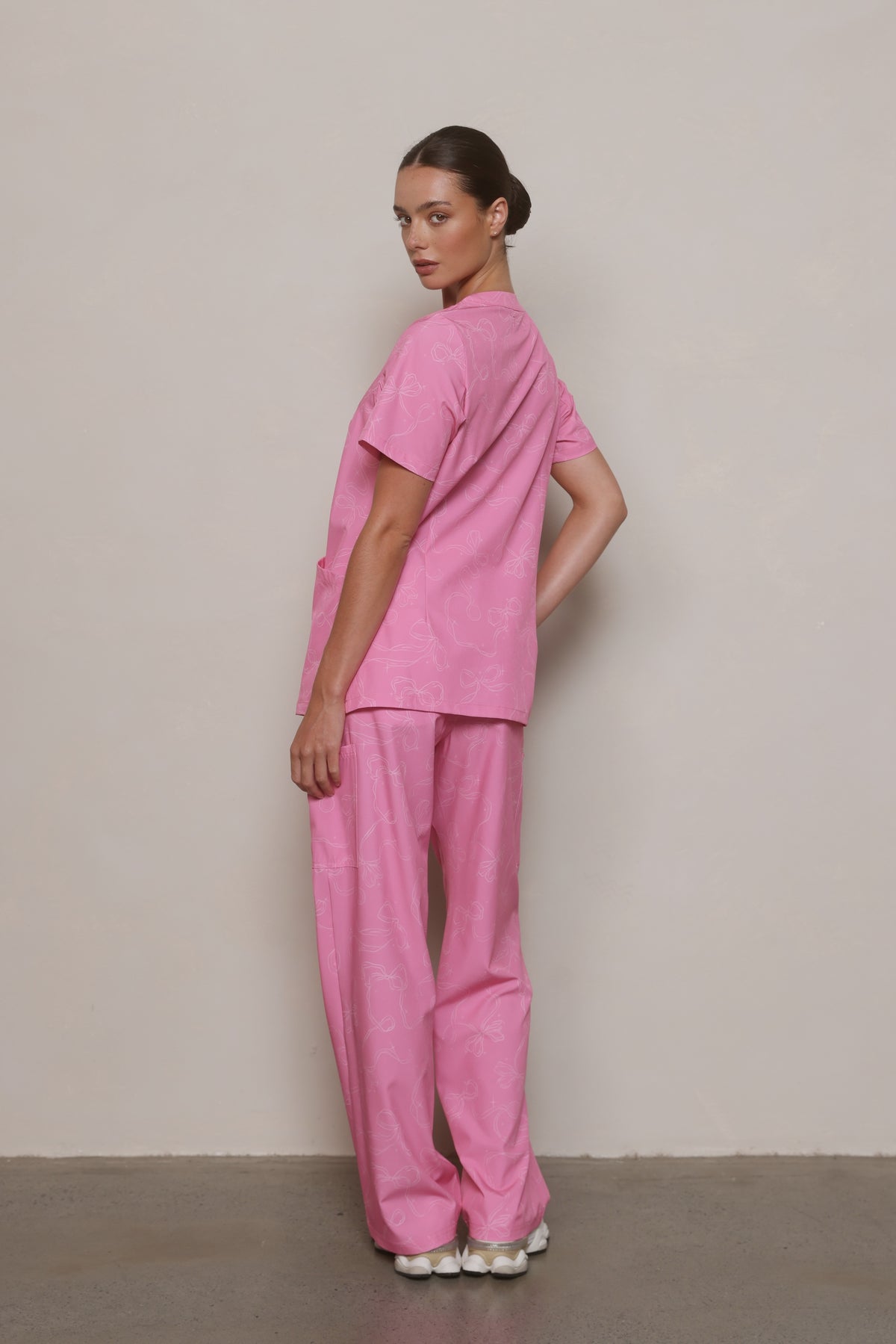 Side view of a model wearing a Hero Scrubs pink printed scrub set, looking over her shoulder.