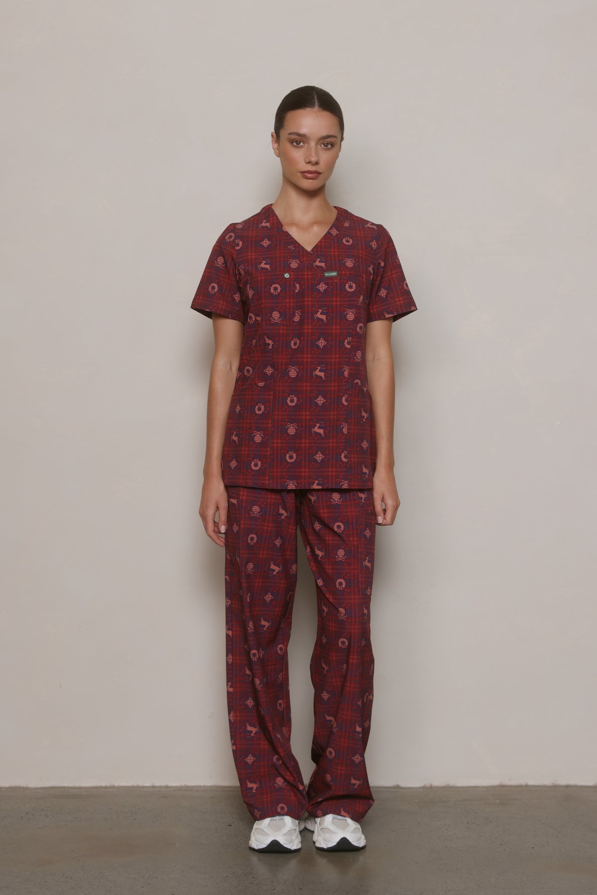 Front view of a model wearing a burgundy Christmas-print Hero Scrubs top and matching pants.