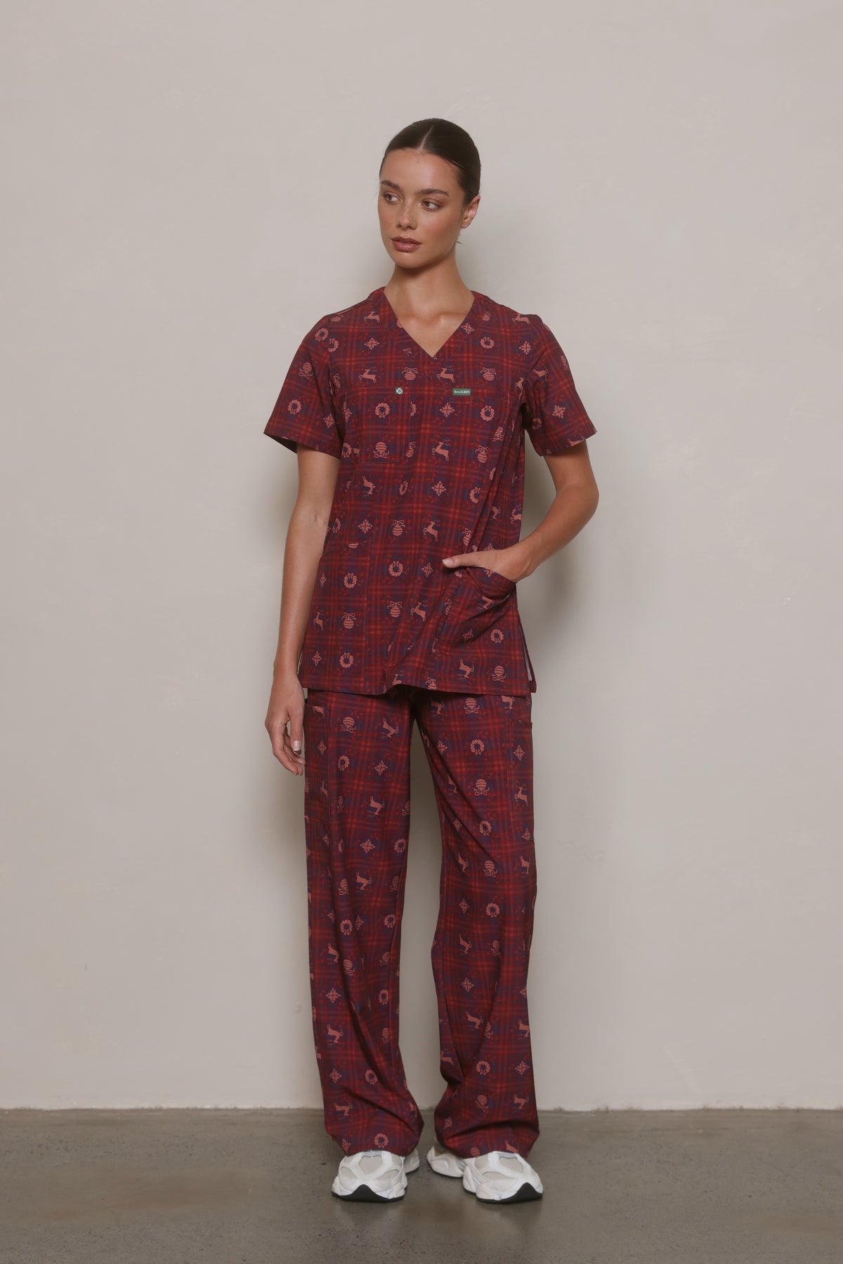 Model wearing a burgundy Christmas-print Hero Scrubs set with one hand in the front pocket.