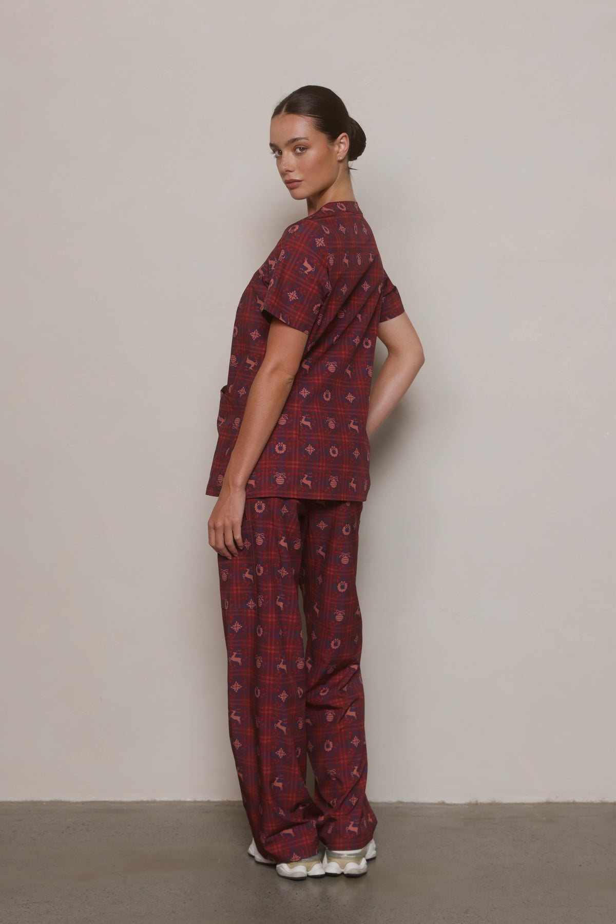Side view of a model wearing a burgundy Christmas-print Hero Scrubs set.