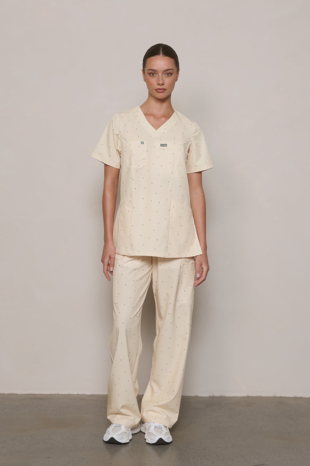 Model wearing a Hero Scrubs yellow printed V-neck top and matching pants, viewed from the front.