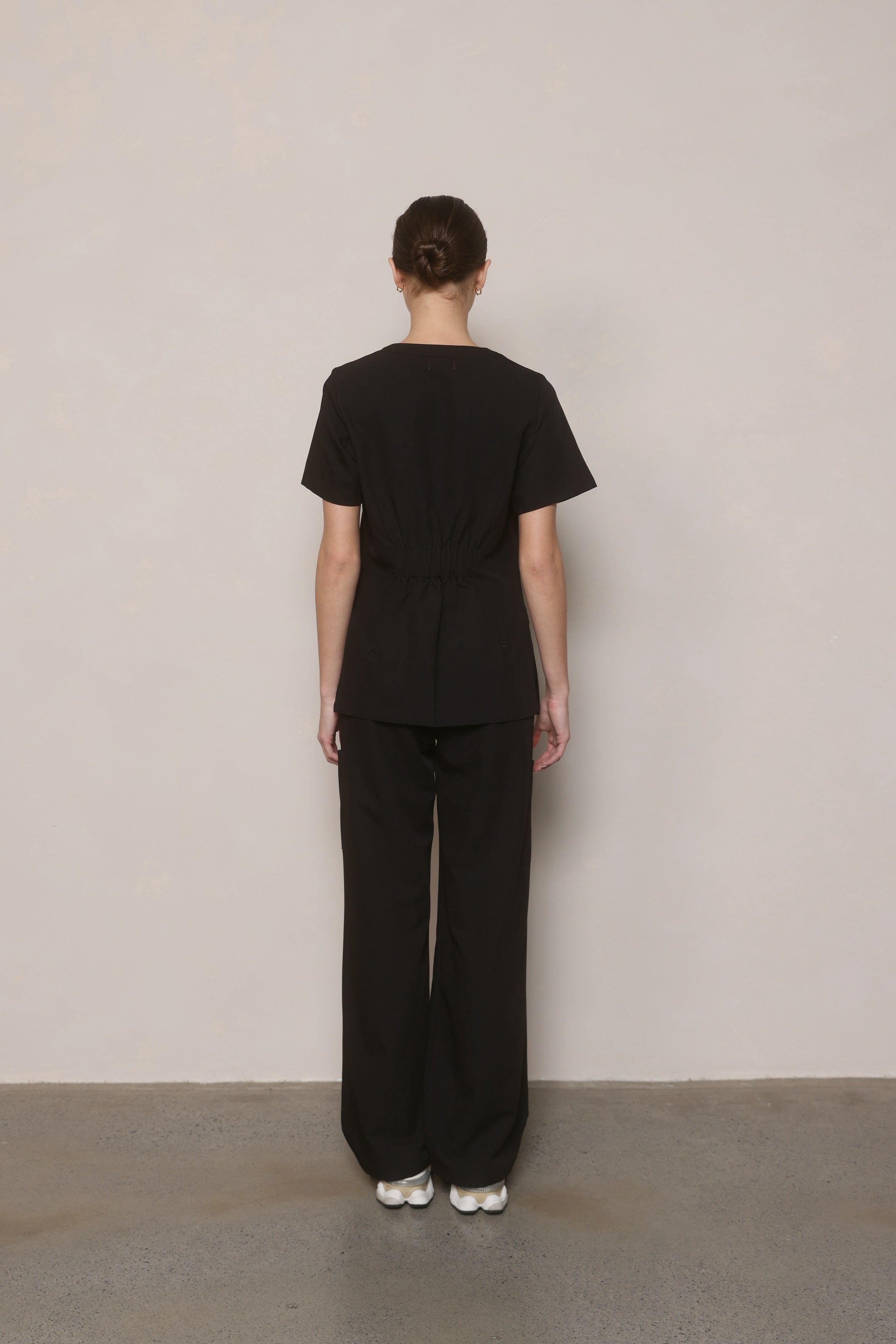 Model standing back-on wearing Hero Scrubs Black scrub top and pants