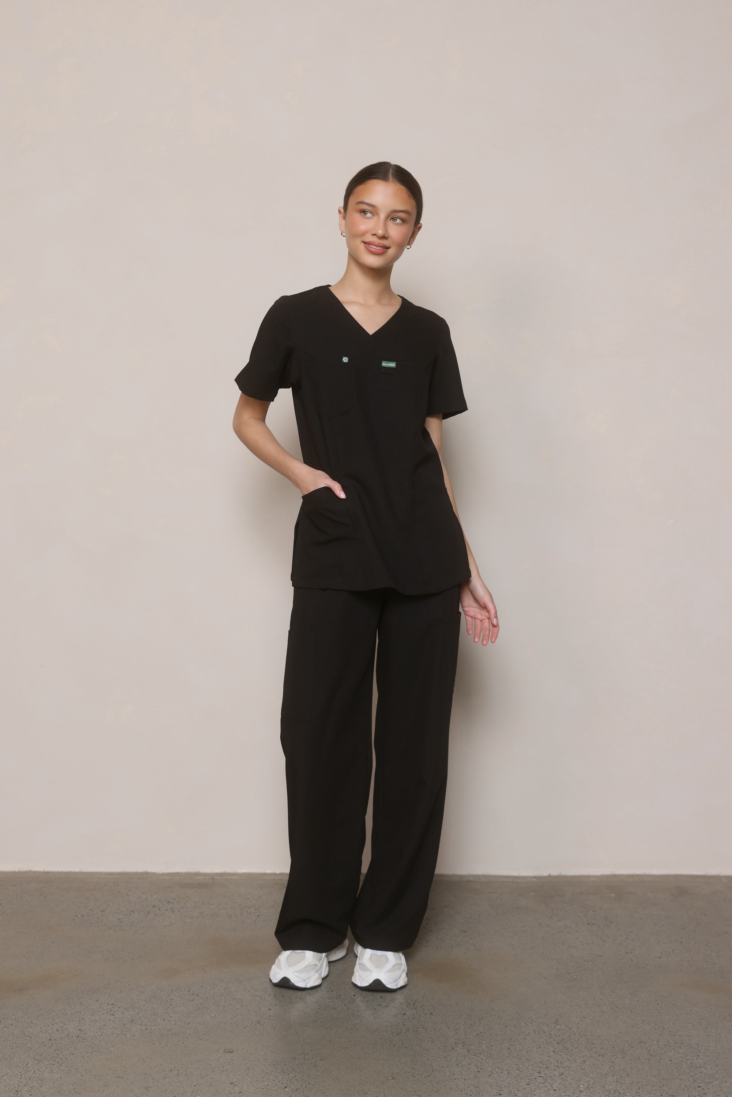 Model standing with hand on hip wearing Hero Scrubs Black women’s scrub set