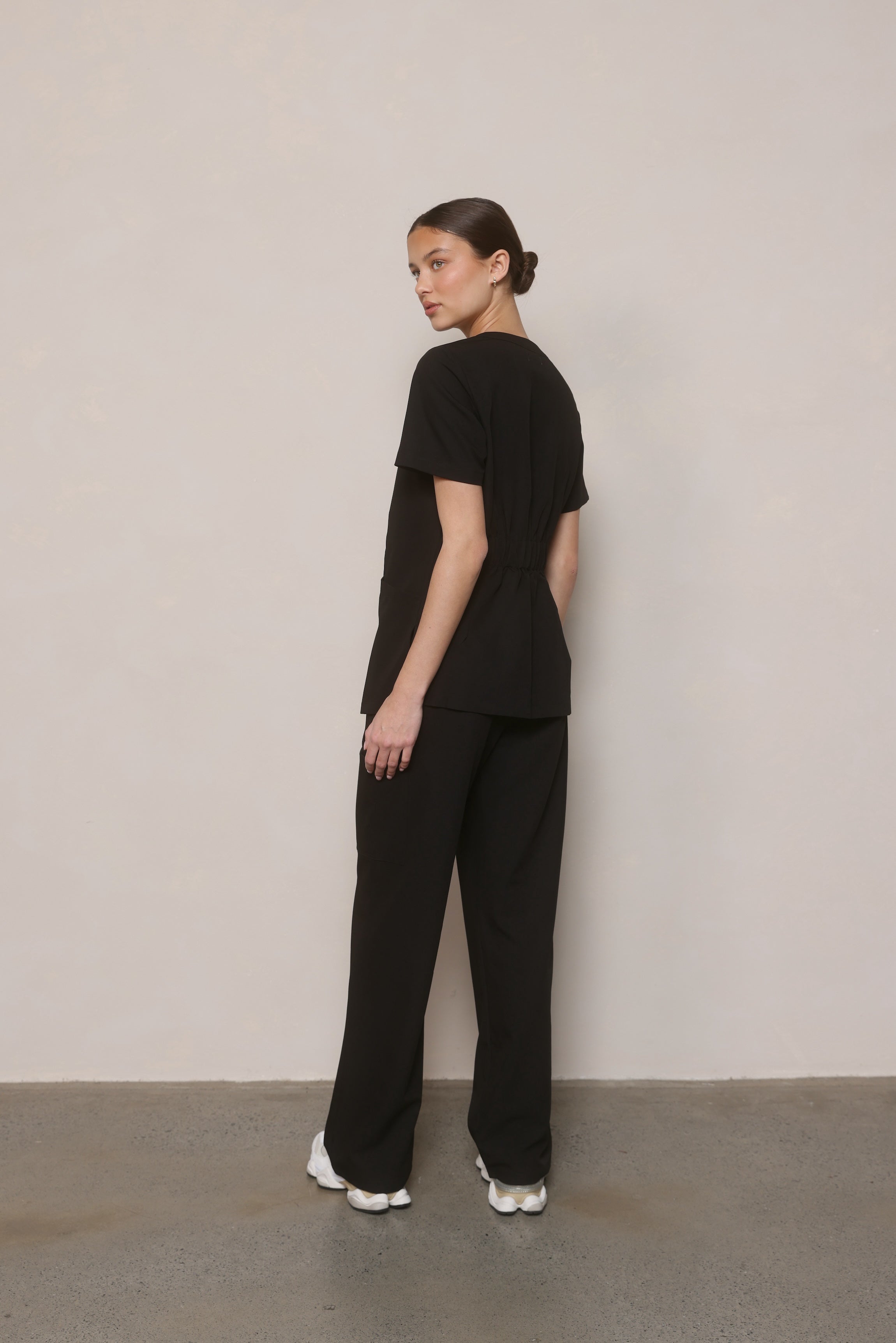 Model in a side-back pose wearing Hero Scrubs Black women’s scrub set