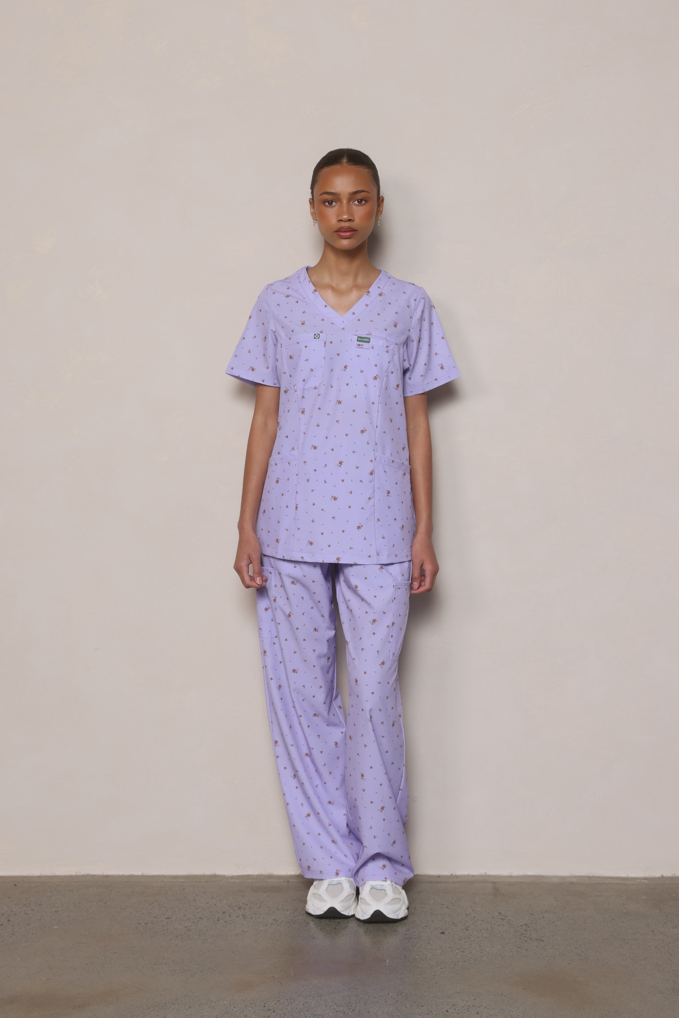 Model standing front-on wearing Hero Scrubs lilac scrub top and pants