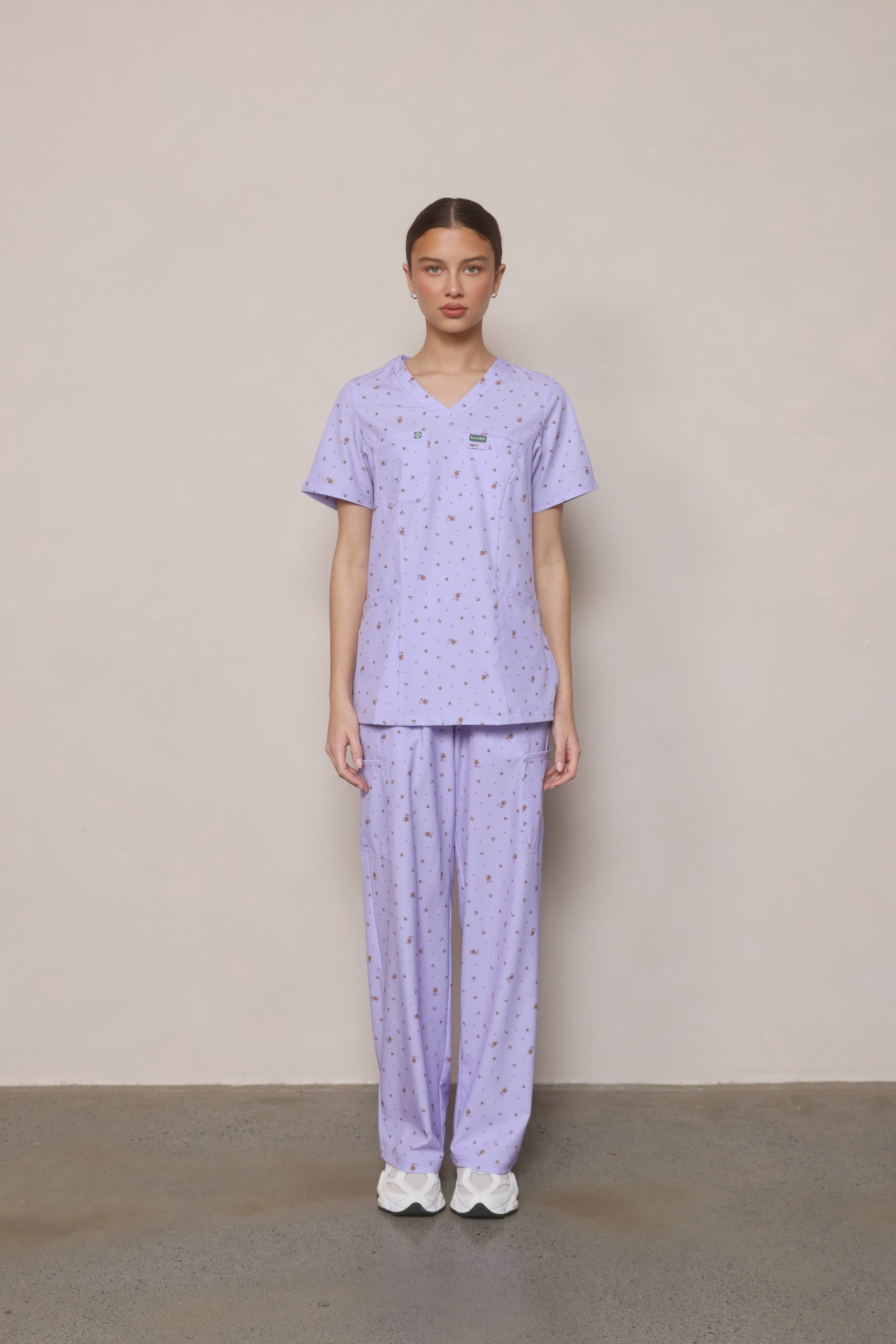 Model standing front-on wearing Hero Scrubs lilac printed scrub set
