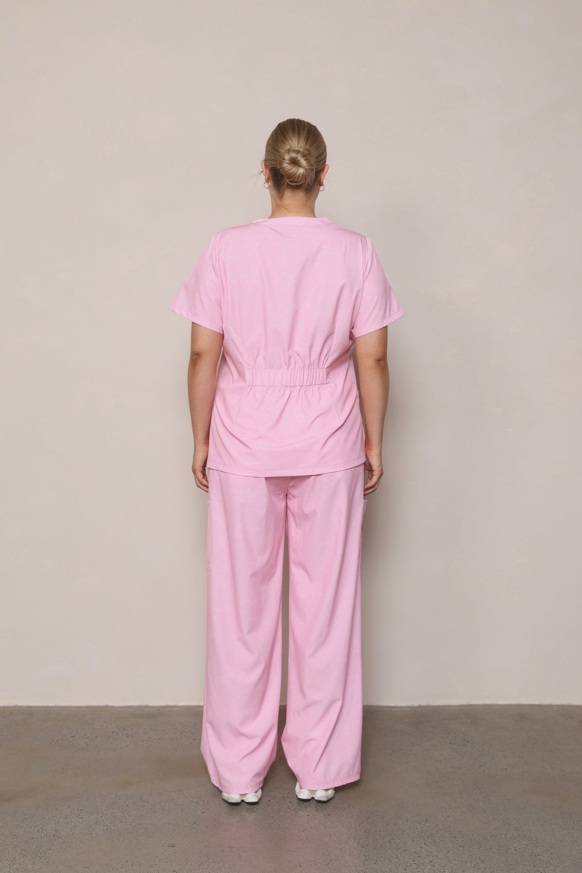 Model standing back-on wearing Hero Scrubs Pink scrub top and pants