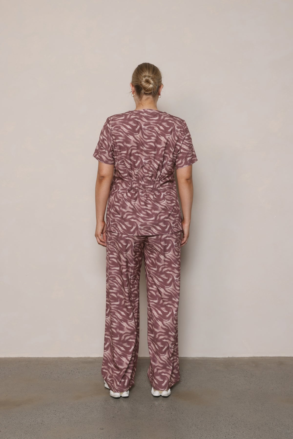 Model standing back-on wearing Hero Scrubs Zebra women’s scrub set